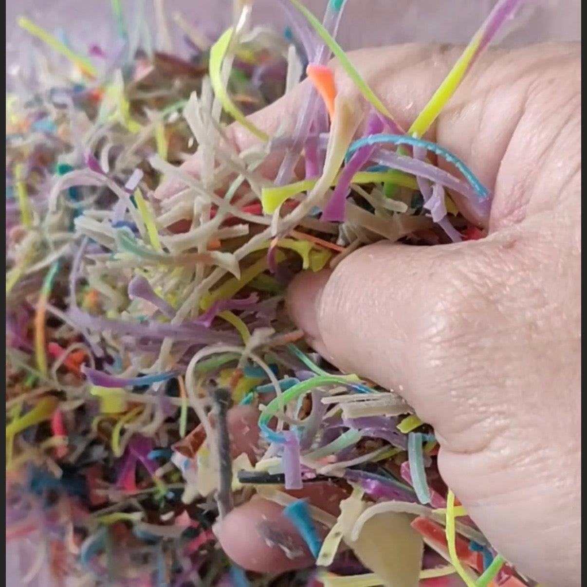 A close-up of a hand holding a pile of shredded, colourful soap confetti .
