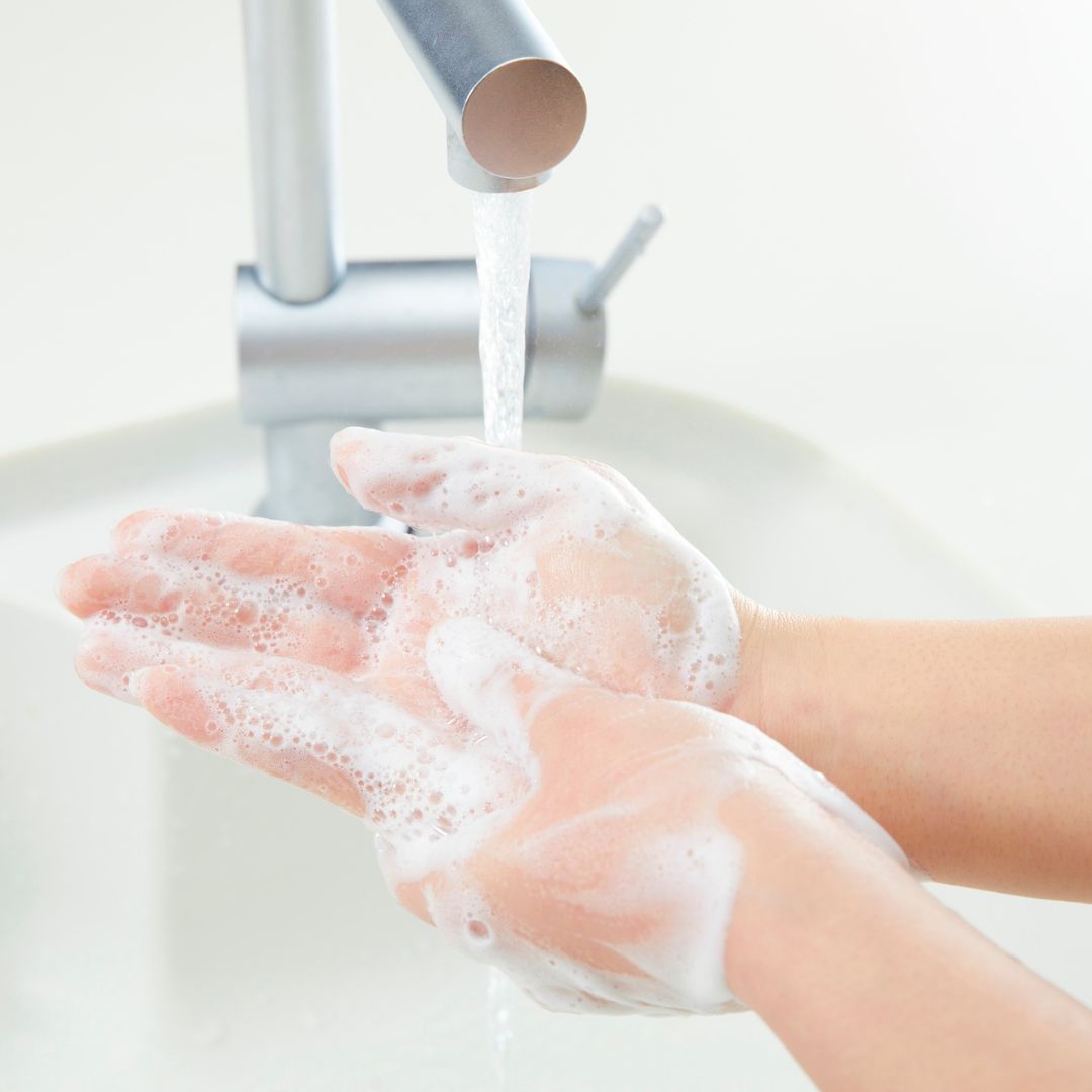 Close-up of a person washing their hands under running water from a modern chrome faucet, with soap lather covering the palms and fingers.