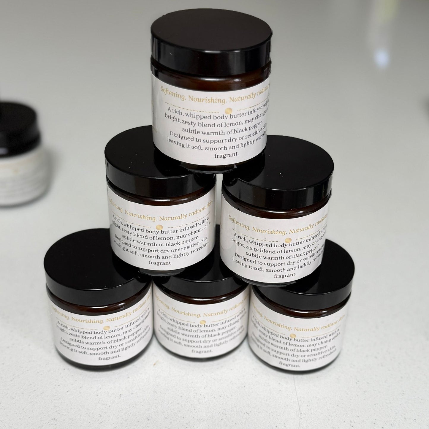 Six amber glass jars of Ita's Natural Essentials Citrus Delight Whipped Body Butter stacked in a pyramid – handmade natural body butter with lemon, may chang and black pepper essential oils, made in small batches in Lancashire