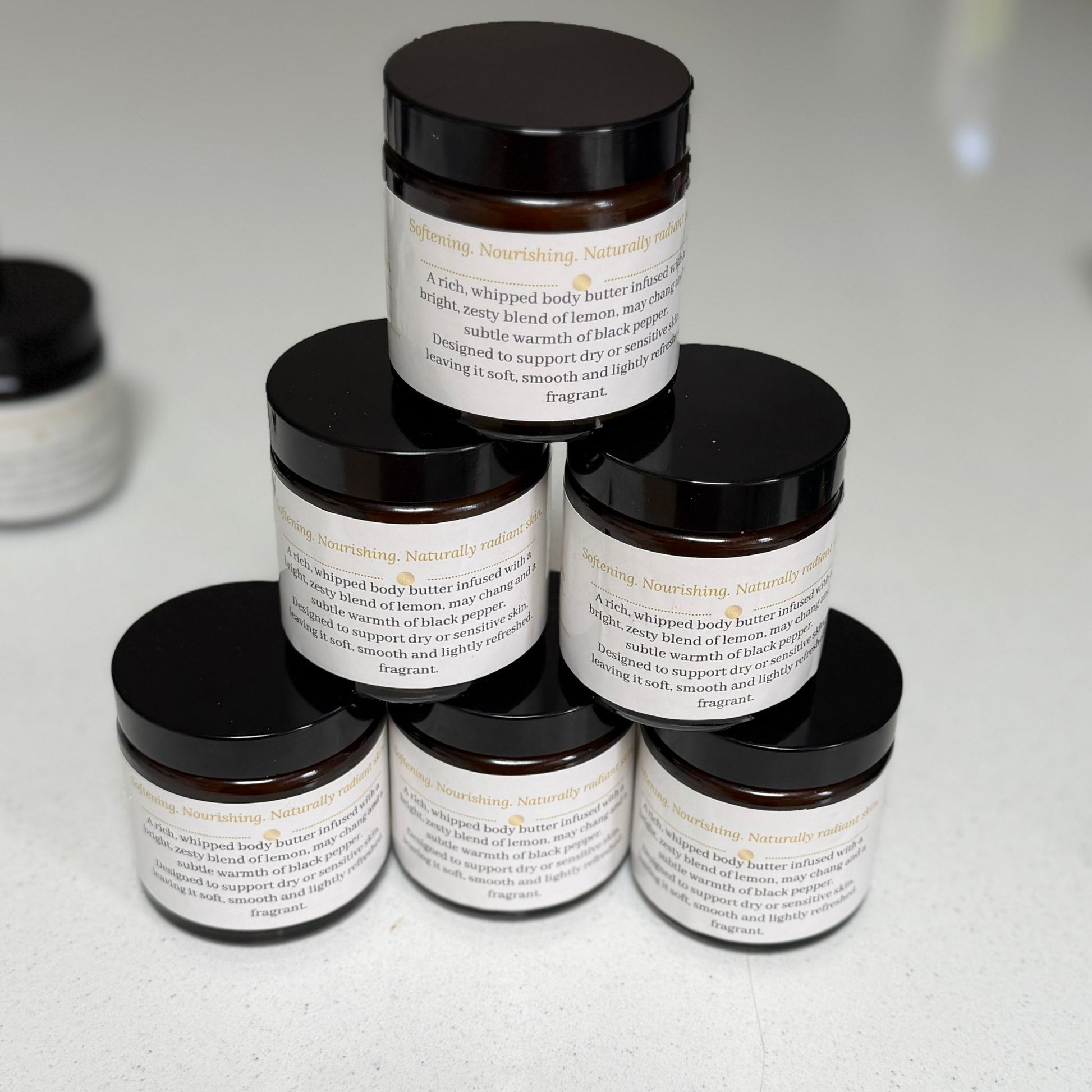 Six amber glass jars of Ita's Natural Essentials Citrus Delight Whipped Body Butter stacked in a pyramid – handmade natural body butter with lemon, may chang and black pepper essential oils, made in small batches in Lancashire