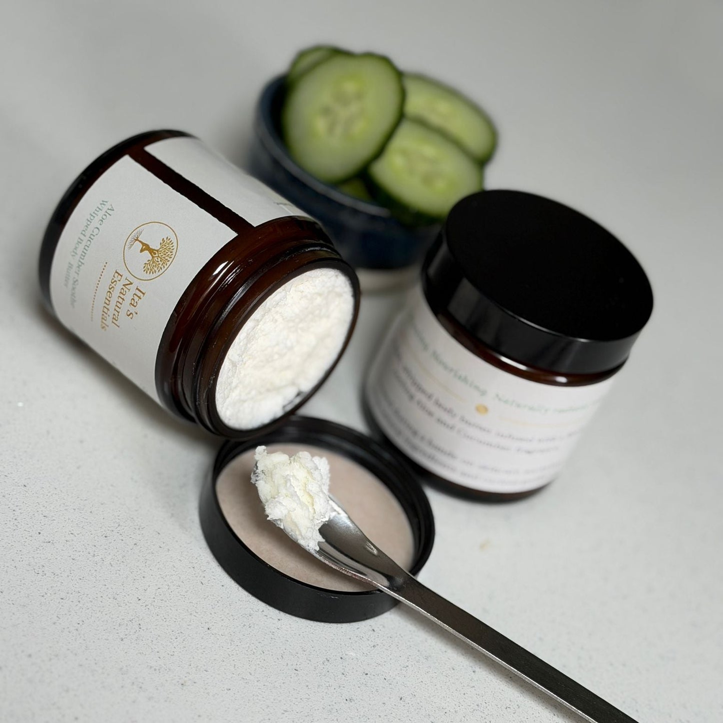 Open jar of Aloe & Cucumber Whipped Body Butter showing its rich whipped texture, with a spoonful of body butter and fresh cucumber slices in the background.