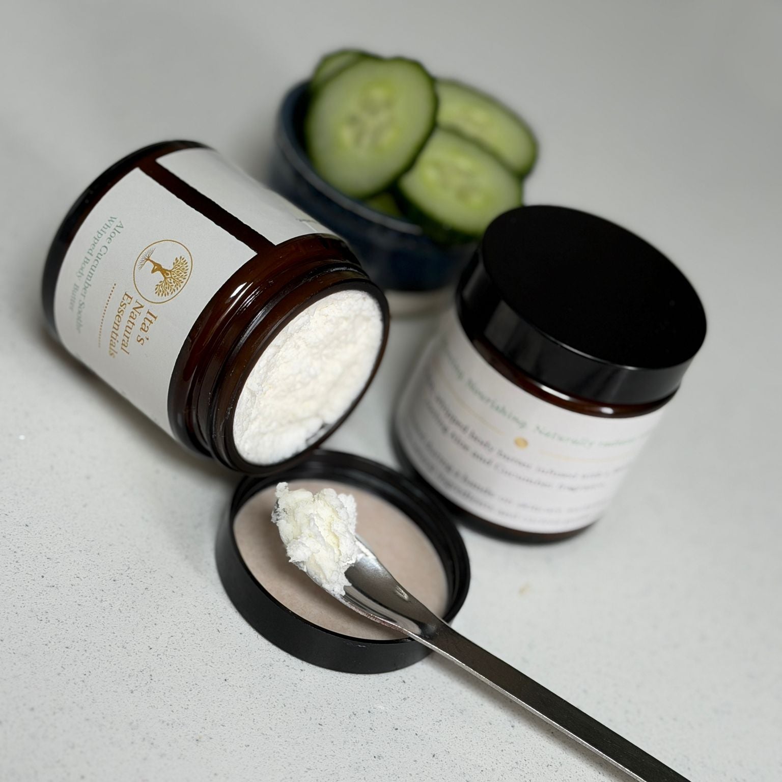 Open jar of Aloe & Cucumber Whipped Body Butter showing its rich whipped texture, with a spoonful of body butter and fresh cucumber slices in the background.